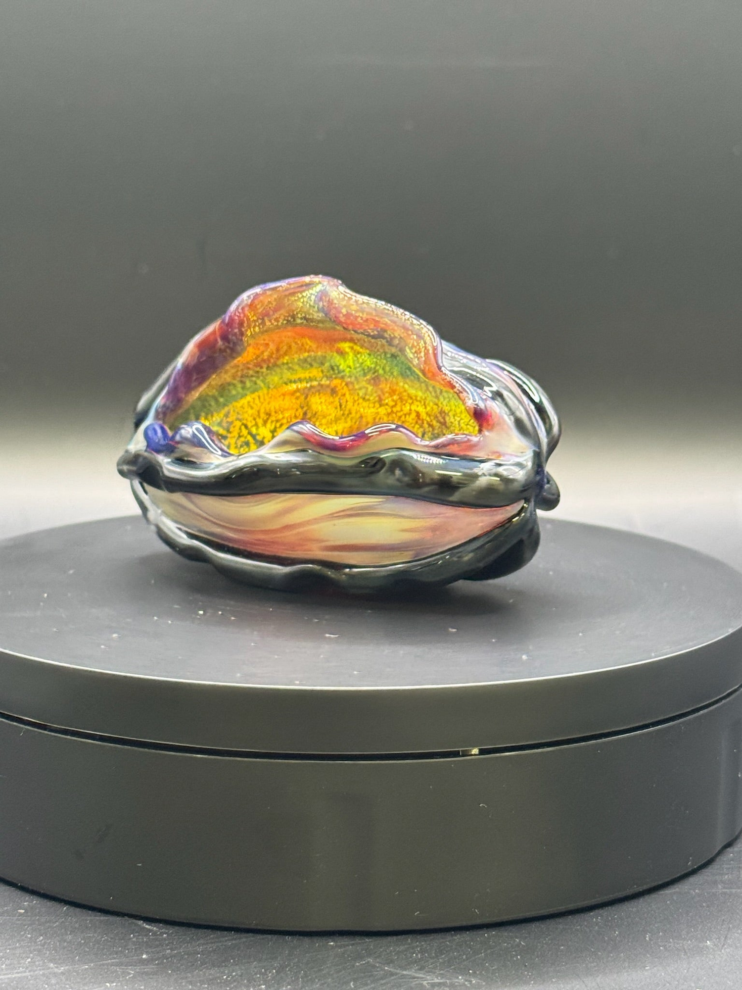 borosilicate glass clam shell made with dichroic glass backed with amber purple and black accents. 